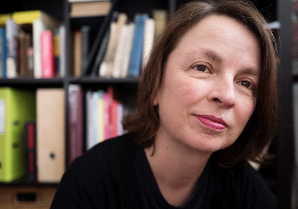 Author Louise Bassett standing in front of a crowded bookcase.